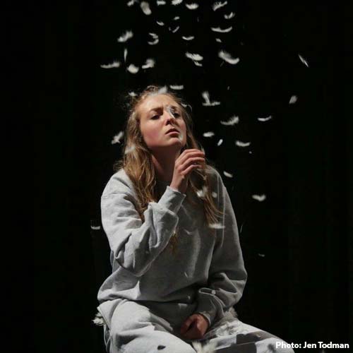 Performer kneeling on floor blowing feathers from hand