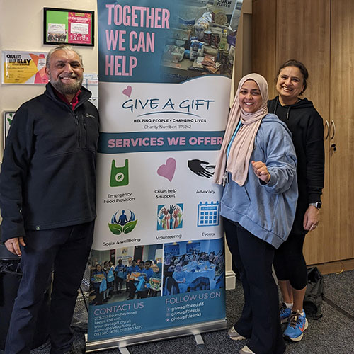 Give a Gift roller banner with three people standing in front of it smiling