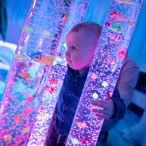 Baby looking between two glow in the dark columns with fish in them. Part of Theatre Hullabaloo.