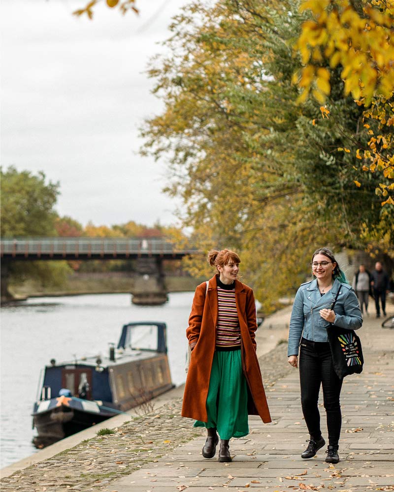 Two students walk together by the river in York city centre.