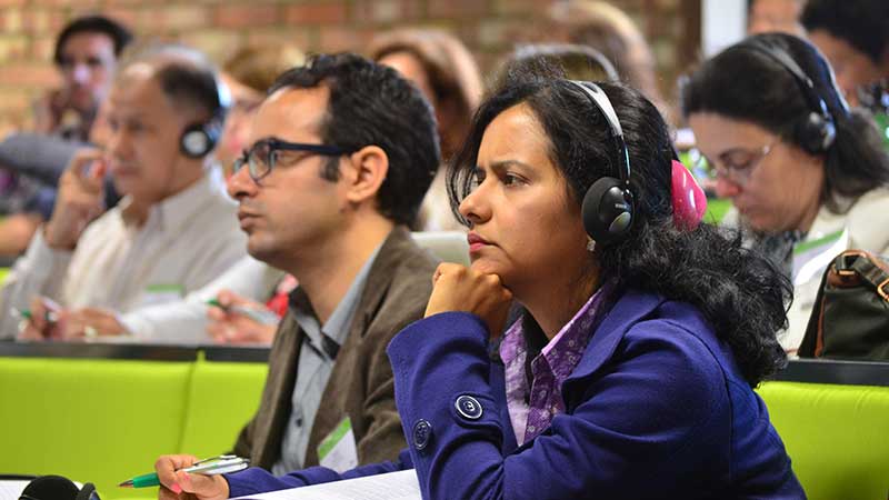 A woman and a man sitting listening. The woman has translation headphones on